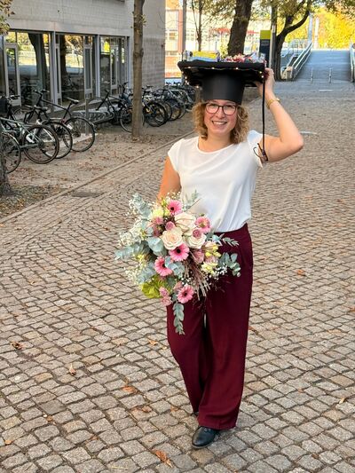 a person (Nadia Günther) holding a bouquet of flowers and wearing a mortarboard