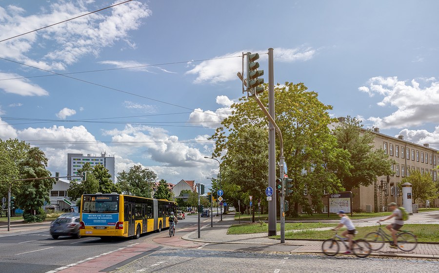 The picture shows an intersection at the TU Dresden campus with cyclists, buses and cars passing by