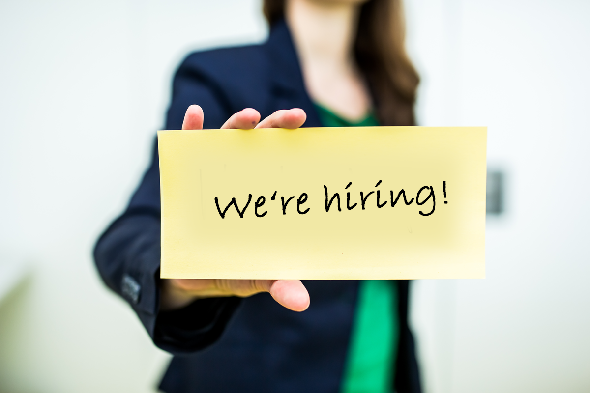 woman holding a sheet of paper with text "we're hiring"